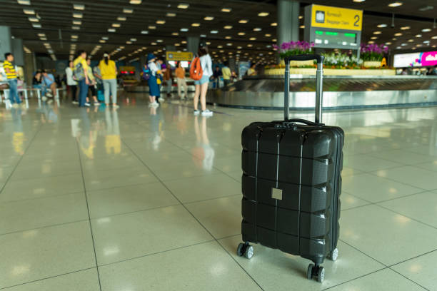 bagagli a rotelle a mano a guscio rigido nero smarriti lasciati incustoditi nell'area di recupero bagagli in aeroporto - hardshell foto e immagini stock