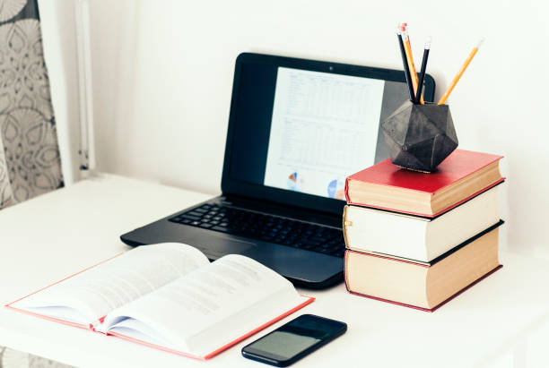 istock Laptop, stack of books, smartphone, notebook and pencils in concrete holder on white table in office business background for education learning concept 1147247516