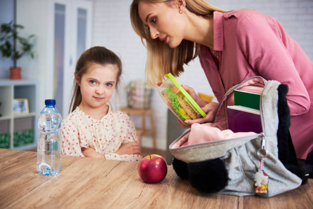 istock Mother putting lunch box with healthy food in daughter's backpack 1147249531