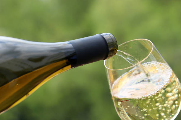 White wine pouring from the bottle into the glass on green nature blurred background Concept of celebration, party, wine drinking outdoors, champagne tasting at winery chardonnay grape stock pictures, royalty-free photos & images
