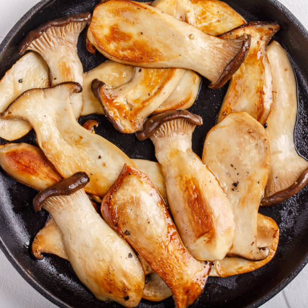 Fried eryngii mushrooms in cast-iron pan on white table. Grilled slices of king oyster mushrooms. Top view, close-up.