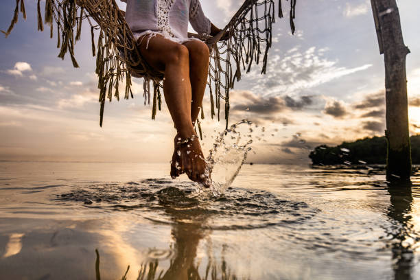 Unrecognizable woman relaxing in hammock above the sea and splashing water with her feet.