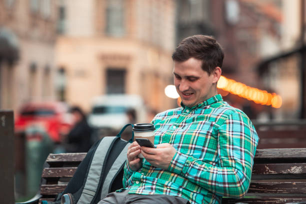 istock portrait of young smiling handsome man sitting on bench drinking coffee browsing internet via phone 1147276718