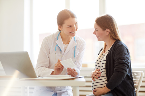 Portrait of female obstetrician smiling at pregnant woman in doctors office, copy space