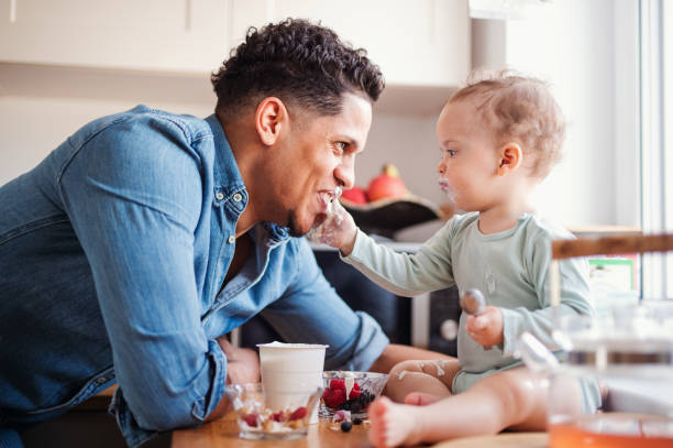 집에서 실내에서 과일과 요구르트를 먹는 아버지와 작은 유아 아들. - domestic kitchen father eating child 뉴스 사진 이미지