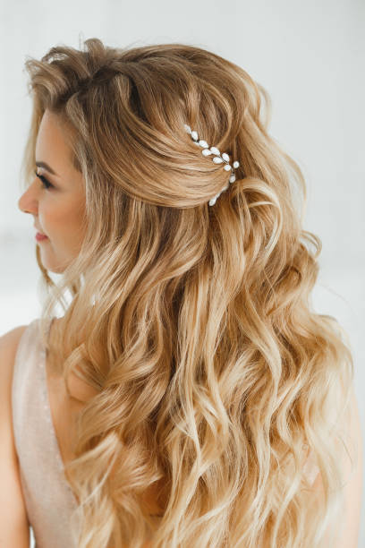 beautiful blonde woman showing her perfect greek hairstyle and purple colored crystal earrings with beads. in beige posing in studio room - women bride personal accessory adult imagens e fotografias de stock