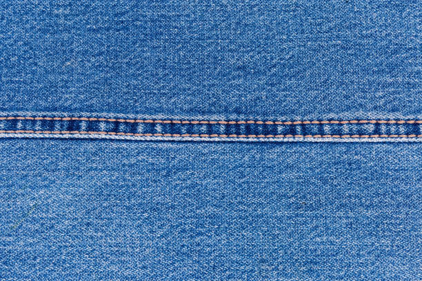 Background of the indigo denim fabric.  Fragment of the jeans with a double stitch made with yellow threads and located horizontally, close-up
