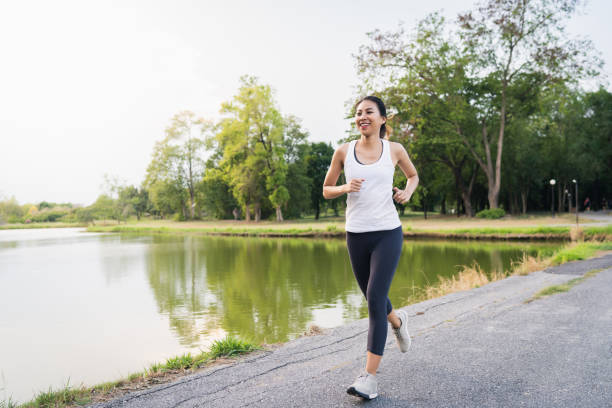 belle jeune femme de coureur asiatique en bonne santé dans les vêtements de sport en cours d’exécution et de jogging sur le trottoir près du lac au parc le matin. fitness de style de vie et les femmes actives exercice dans la ville urbaine concept. - running jogging asian ethnicity women photos et images de collection