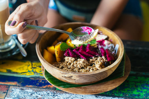 Woman's hands with smoothie bowl made with mango, banana, granola, grated coconut, dragon fruit and mint Woman's hands with smoothie bowl made with mango, banana, granola, grated coconut, dragon fruit and mint. Concept breakfast, healthy food eating chia seeds stock pictures, royalty-free photos & images