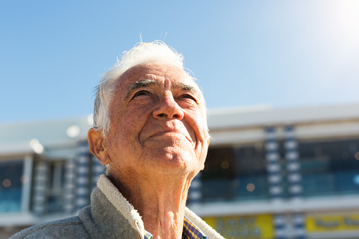 A senior man enjoys his retirement, standing outdoors and smiling up at the sunny sky.