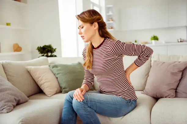 Photo of Close up side profile photo beautiful she her lady arms hands hold back spine suffering terrible pain wear jeans denim striped pullover clothes bright comfort flat house living room indoors