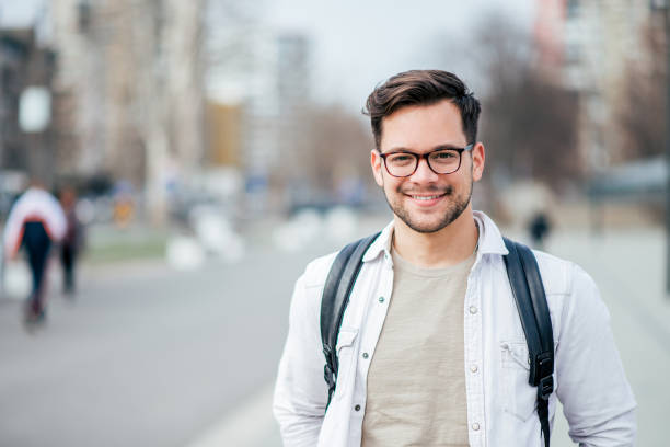 街の通りで笑顔の学生の肖像画。 - 若い男性一人 ストックフォトと画像