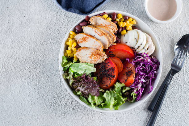 istock Healthy lunch salad with chicken, egg, tomatoes, lettuce, corn, red beans, red cabbage and barbeque sauce on light concrete background. Dietary menu. Flat lay, top view, copy space 1147294252
