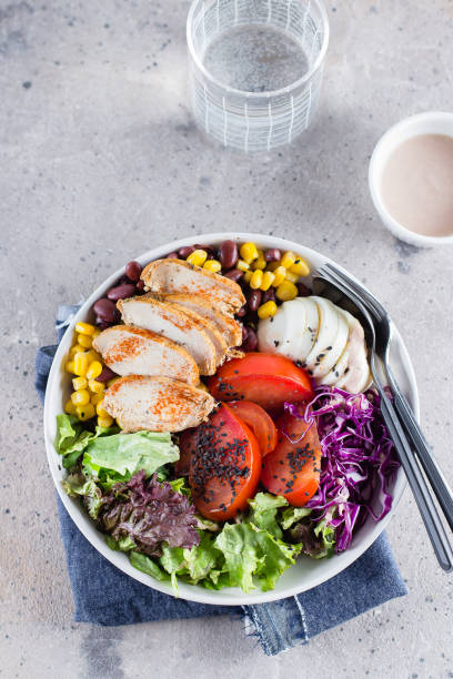 istock Healthy lunch salad with chicken, egg, tomatoes, lettuce, corn, red beans, red cabbage and barbeque sauce on light concrete background. Dietary menu. Flat lay, top view 1147294327