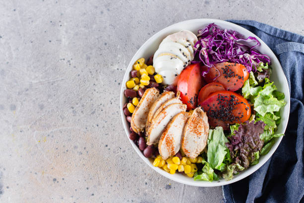 istock Healthy lunch salad with chicken, egg, tomatoes, lettuce, corn, red beans, red cabbage and barbeque sauce on light concrete background. Dietary menu. Flat lay, top view 1147294340