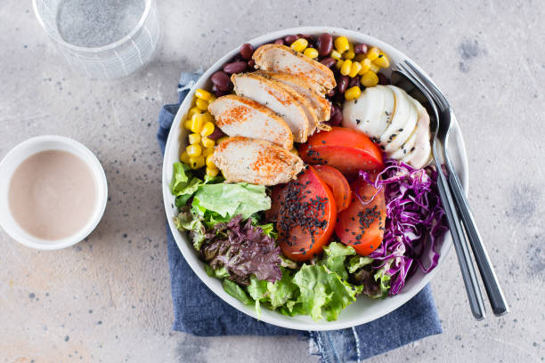 istock Healthy lunch salad with chicken, egg, tomatoes, lettuce, corn, red beans, red cabbage and barbeque sauce on light concrete background. Dietary menu. Flat lay, top view 1147294345