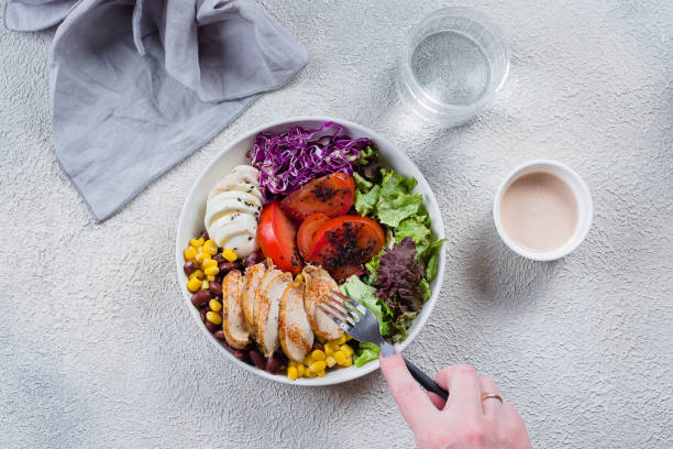 la femme mange un déjeuner sain. bol avec poulet, oeuf, tomates, laitue, maïs, haricots rouges, chou rouge et sauce barbecue. nourriture propre et concept de nutrition diététique. vue de dessus, espace de copie, lay plat - water women glass healthy eating photos et images de collection