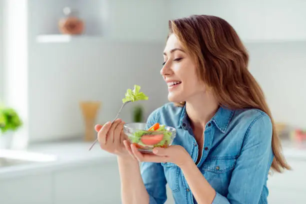 Close-up portrait of her she nice-looking sweet lovely charming cute attractive cheerful cheery positive brown-haired lady tasting new salad mix farm vegs in light white interior style kitchen.
