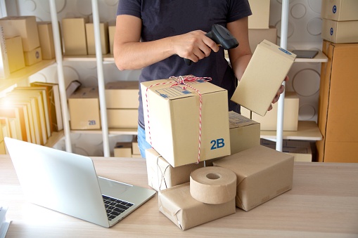 Courier scanning cardboard box with barcode scanner in warehouse. Close up of warehouse manager hand scanning boxes with barcode reader. Woman using bardode reader reading and scanning labels on boxes