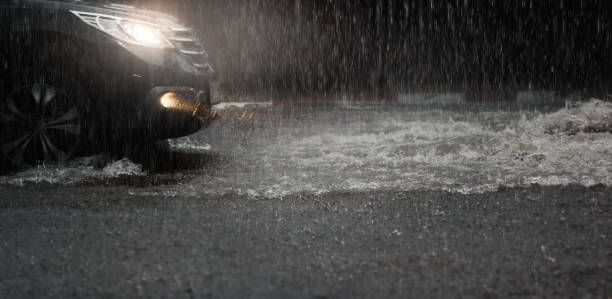 la voiture avec des phares traversent l’eau d’inondation après que la pluie dure tombent la nuit. - night wet road street photos et images de collection