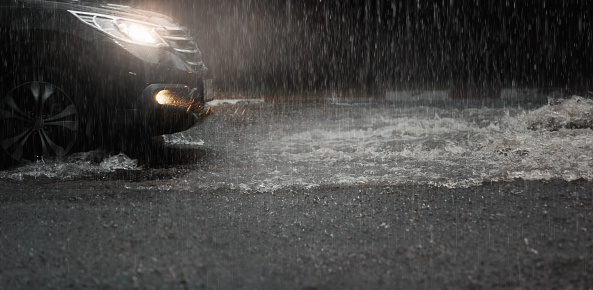 Car with headlights run through flood water after hard rain fall at night.Rainy season.
