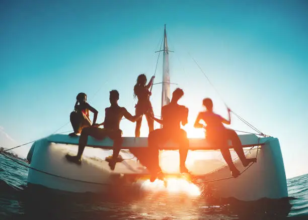 Silhouette of young friends chilling in catamaran boat - Group of people making tour ocean trip - Travel, summer, friendship, tropical concept - Focus on two left guys - Water on camera