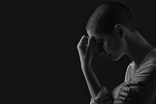Sad, frightened and depressed female cancer patient portrait on dark background with copy space. Breast cancer patient, head in hands, black and white portrait.