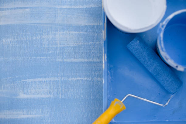 istock blue and white paint in cans top view. roller with a yellow handle for painting walls 1147301717