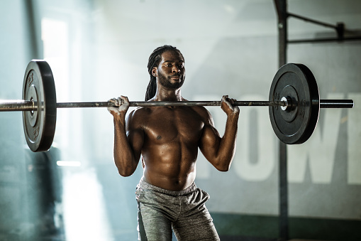Young black athlete having weight training with barbell in a health club.