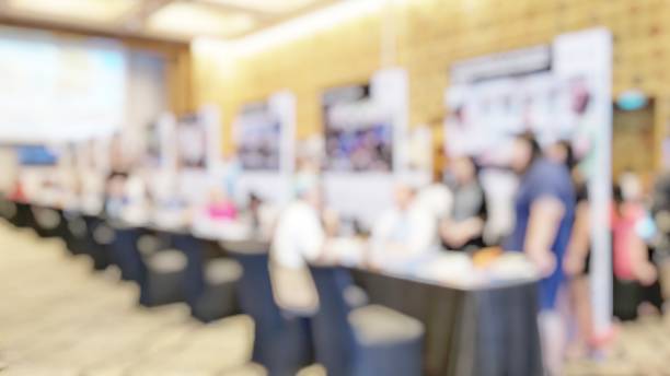 Blur background consultant helping parents/students with educational planning in education fair. Blurry booths of school or company for people to find school or job in career expo in lobby hall.