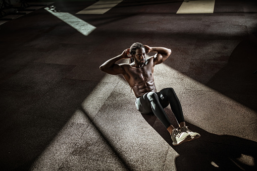 High angle view of African American male athlete exercising sit-ups with hands behind his head in a gym. Copy space.