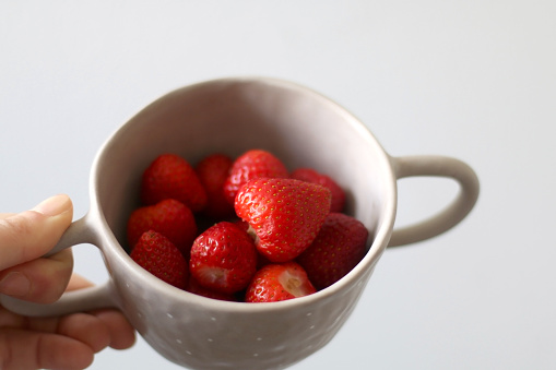 Unrecognizable person holding a bowl of strawberries. Selective focus, white background.