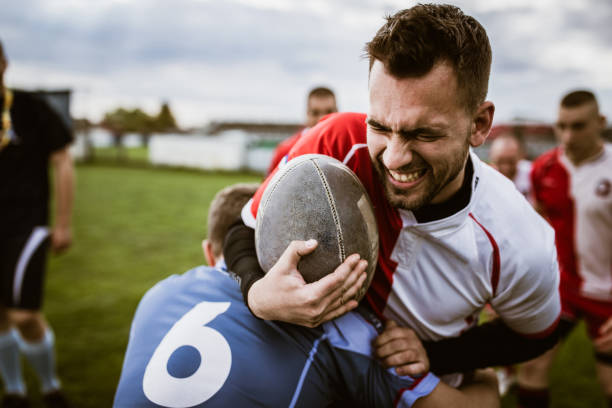 Blocking in rugby match! Determined sportsman with ball being blocked by his opponent during rugby match on a field. offense sporting position stock pictures, royalty-free photos & images
