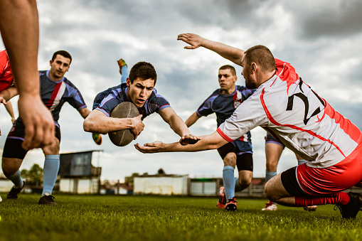 Young rugby player scoring touchdown among his rivals during a match on playing field. Copy space.