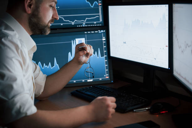 istock Need to grab eyewear. Bearded man in white shirt works in the office with multiple computer screens in index charts 1147314624
