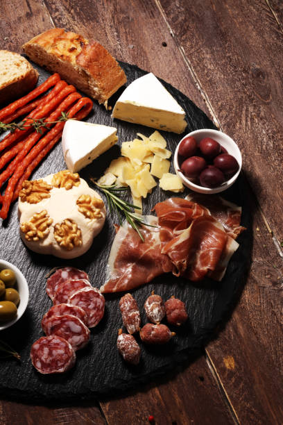 istock Cutting board with prosciutto, salami, cheese,bread and olives on dark stone background 1147316748