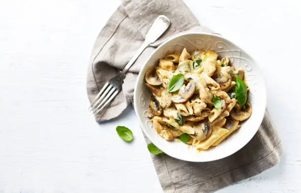 Photo of Penne pasta with mushrooms, chicken, spinach and cream sauce. Mediterranean cuisine. Flat lay. White background