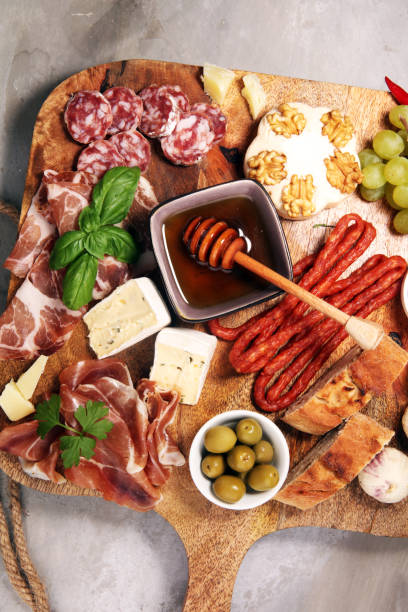 istock Cutting board with prosciutto, salami, cheese,bread and olives on dark stone background 1147319616