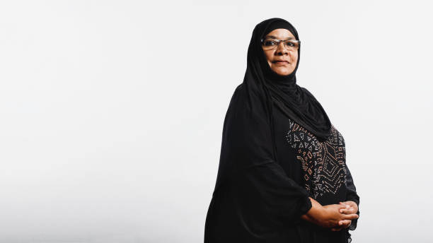 Islamic woman in hijab Senior muslim woman in hijab standing against white background. Arabic woman wearing eyeglasses and a black hijab looking at camera. arab woman stock pictures, royalty-free photos & images