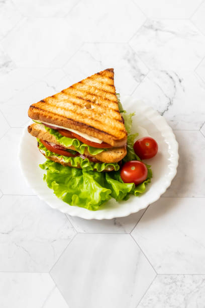 Sandwich with cheese, tomato, cucumber, sausage and salad on a light background. Vertical orientation stock photo