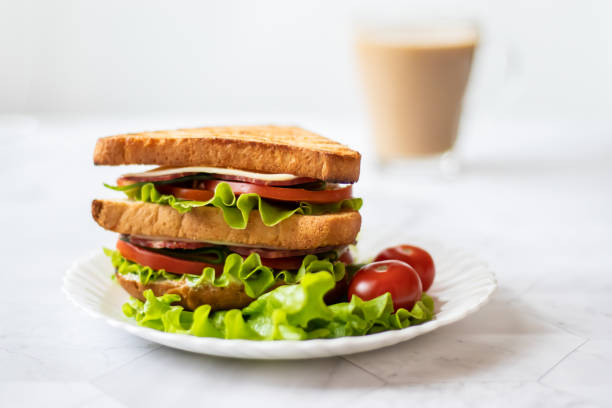 Sandwich with cheese, tomato, cucumber, sausage and salad on a light background. Coffee with milk. Horizontal orientation stock photo