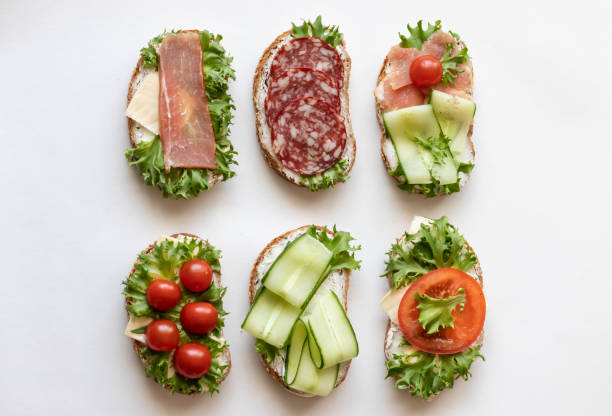 istock Fresh sandwiches with sausage, cheese, bacon, tomatoes, lettuce, cucumbers on a light background. Horizontal orientation 1147323189