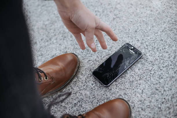 istock Young woman picks up her Broken smartphone with cracked screen glass after falling 1147323402