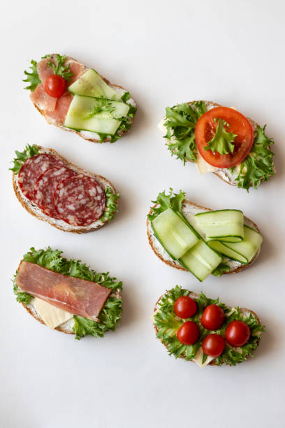 istock Fresh sandwiches with sausage, cheese, bacon, tomatoes, lettuce, cucumbers on a light background. Vertical orientation 1147323531