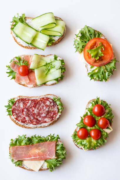 istock Fresh sandwiches with sausage, cheese, bacon, tomatoes, lettuce, cucumbers on a light background. Vertical orientation 1147323550