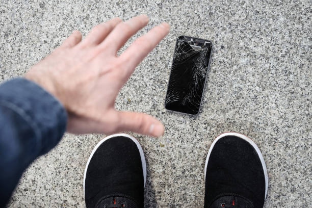 istock Young man picks up his broken smartphone with cracked screen glass after falling 1147324179