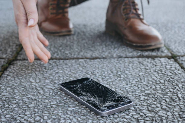 istock Young woman picks up her broken smartphone with cracked screen after falling 1147324191