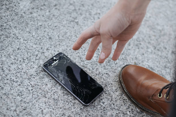 istock Young woman picks up her broken smartphone with cracked screen glass after huge falling 1147324306
