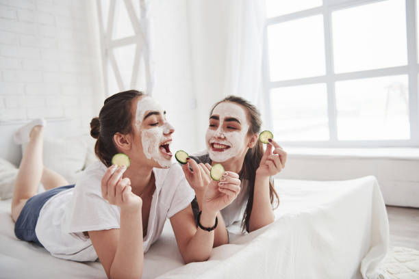 istock Interesting how it's taste. Conception of skin care by using white mask and cucumbers on the face. Two female sisters have weekend at bedroom 1147328124