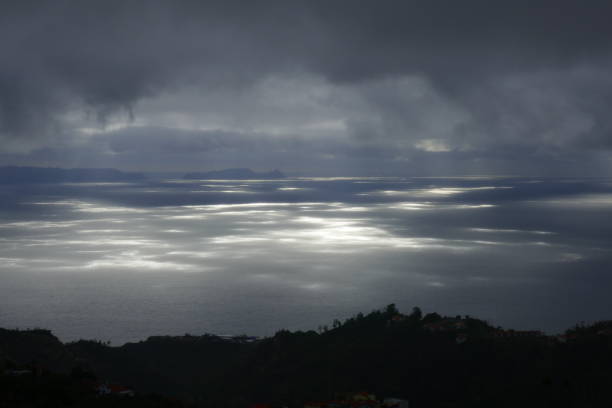 istock Shafts of sunlight slicing through the heavy rain clouds light up sparkling patterns on the sea in Maderia 1147328495